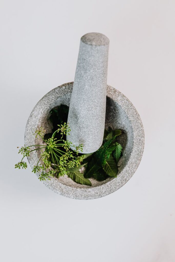 Top view of a stone mortar and pestle grinding fresh green herbs on a white background.